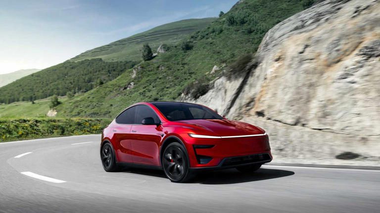 A red Tesla Model Y driving on a mountain road.