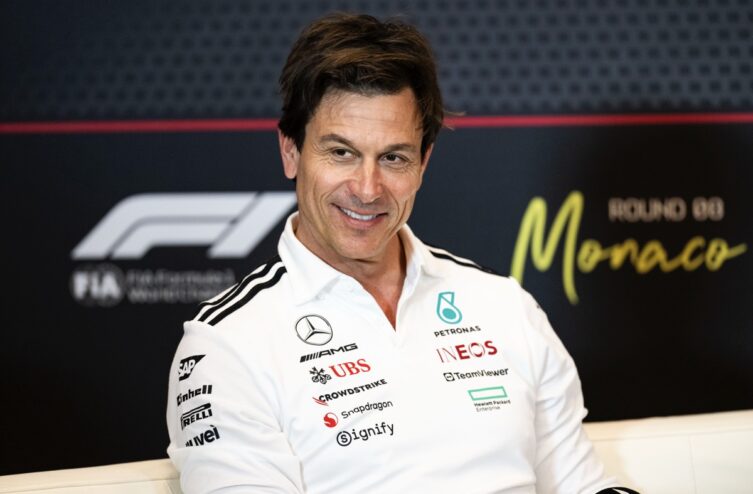 A man in a white Mercedes AMG Petronas F1 team shirt smiling.