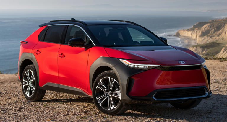 A sleek red electric SUV parked near the coast under a cloudy sky.