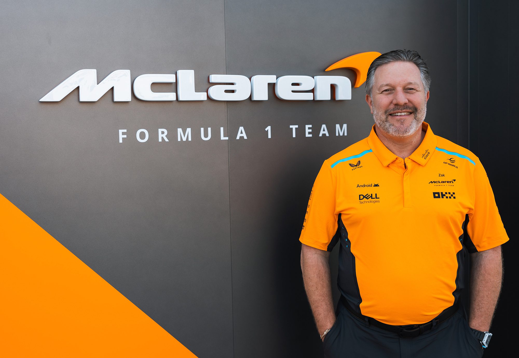 Man smiling next to McLaren Formula 1 Team logo in orange and black shirt.