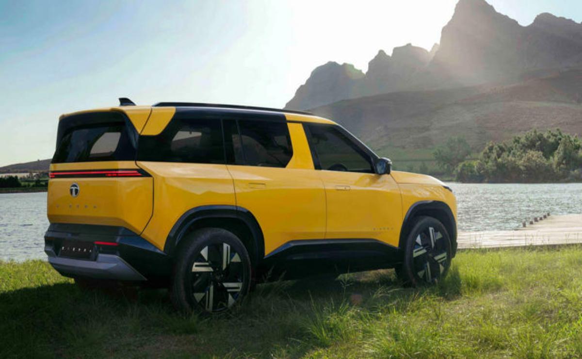 Yellow SUV parked on grassy terrain with mountains in the background.
