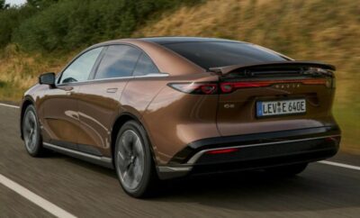 Sleek brown electric sedan driving on a scenic road.