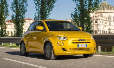A bright yellow compact car driving on a road with trees in the background.