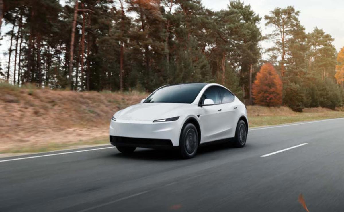 A white Tesla Model Y driving on a road surrounded by autumn trees.