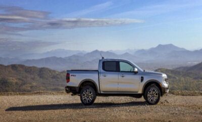 Silver pickup truck parked on a gravel road with mountains in the background.