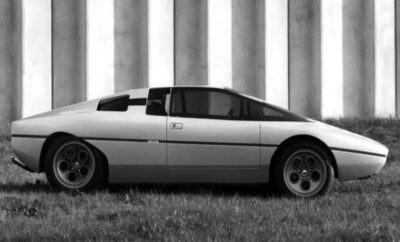 Side view of a vintage sports car parked on grass near large pillars.