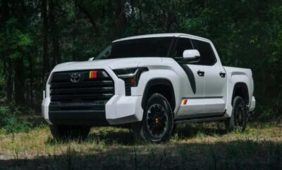 White Toyota pickup truck parked on grass with trees in background.