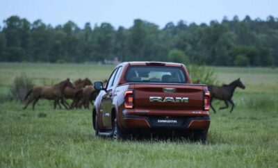 A red RAM truck driving through a grassy field with horses nearby.