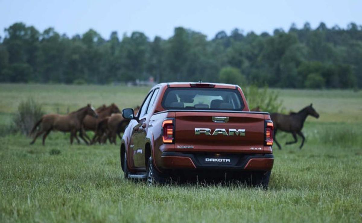 A red RAM truck driving through a grassy field with horses nearby.