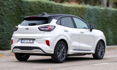 White compact SUV driving on a road near greenery.