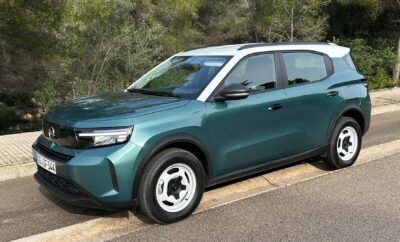 A green SUV parked on a roadside with trees in the background.