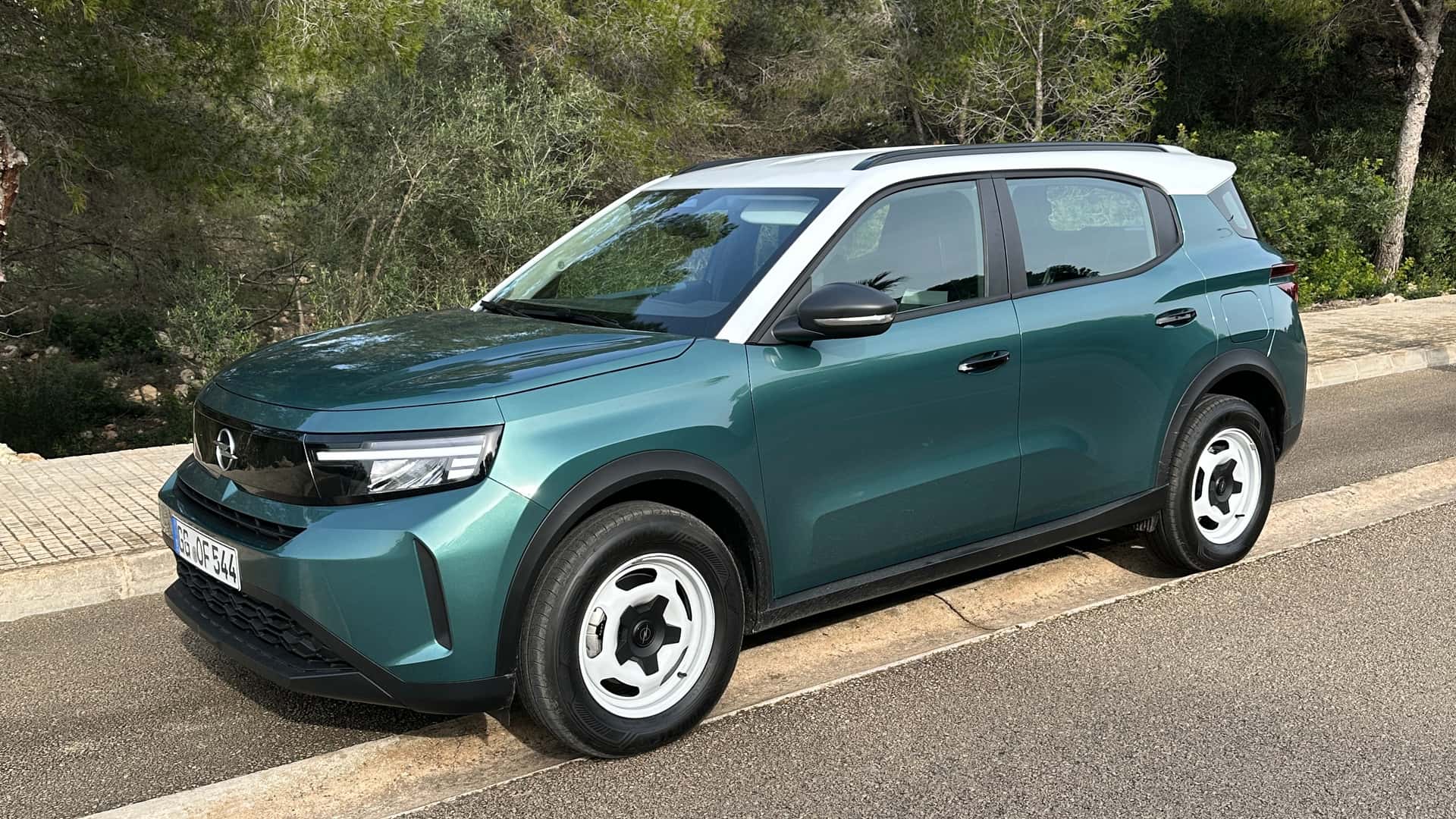 A green SUV parked on a roadside with trees in the background.