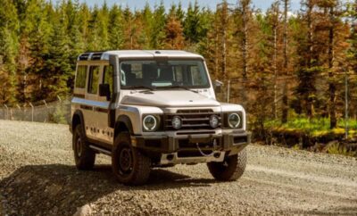 White off-road vehicle driving on a gravel path with trees in the background.