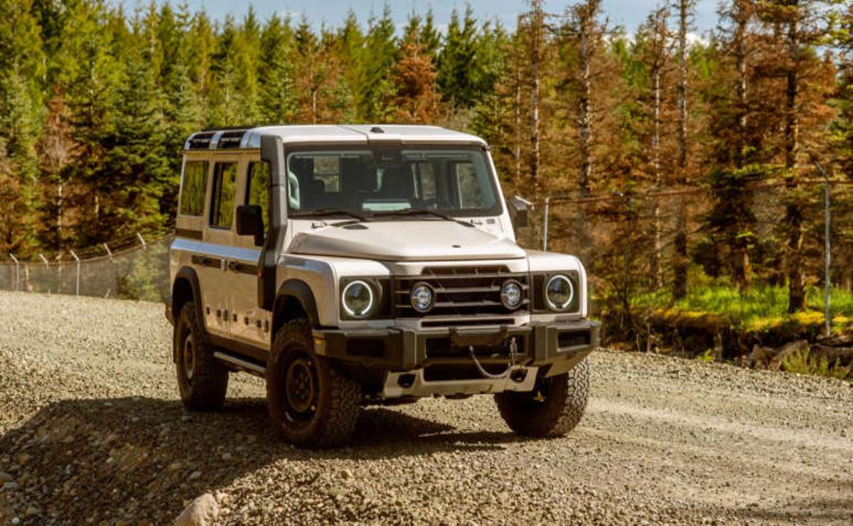 White off-road vehicle driving on a gravel path with trees in the background.