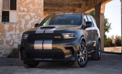 Black Dodge Durango SRT with silver racing stripes parked under a rustic wooden roof.