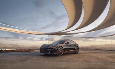 A sleek black sports car parked under a modern circular architectural structure at sunset.