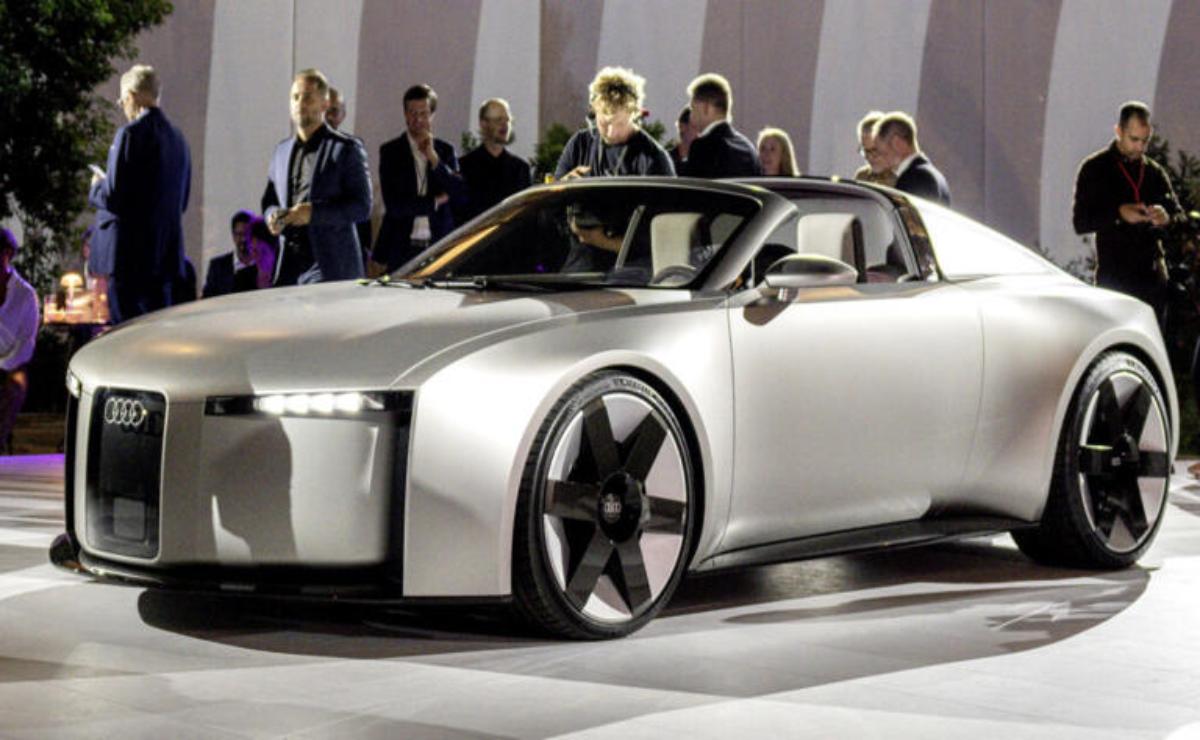 Futuristic silver concept car showcased at an auto event with attendees.