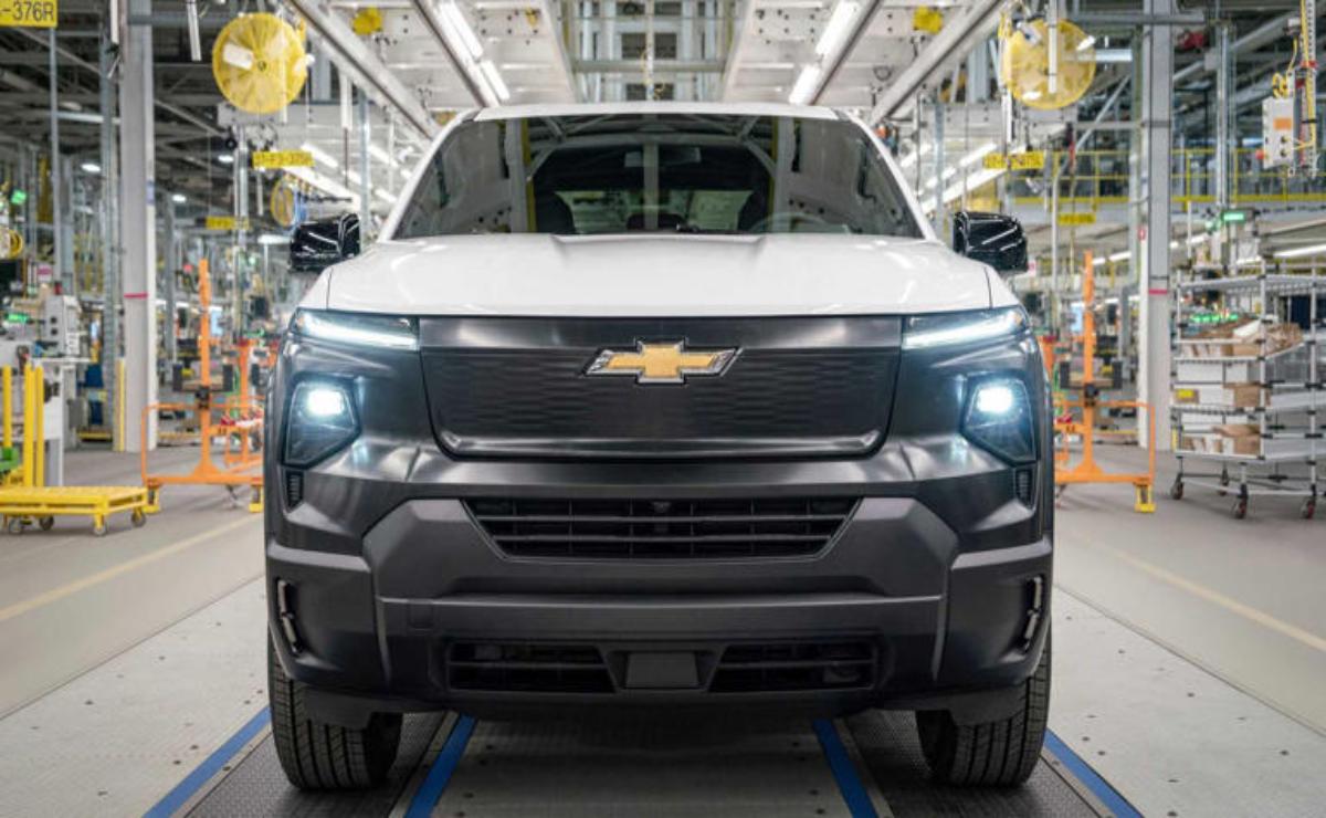 Front view of a white Chevrolet electric truck with headlights on.