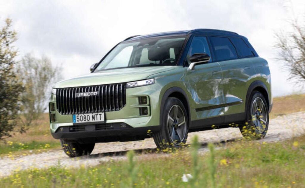 A man working on his laptop and writing in a notebook at a desk.