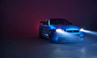 A sleek blue sports car with headlights on in a dark, moody setting.