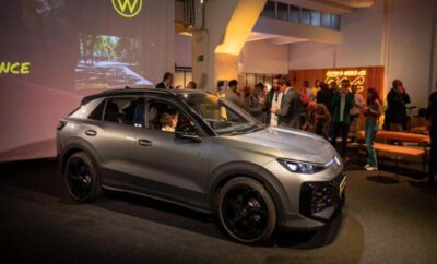A sleek gray car on display with people in the background at an indoor event.