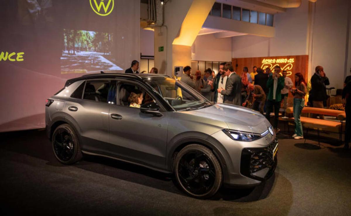 A sleek gray car on display with people in the background at an indoor event.