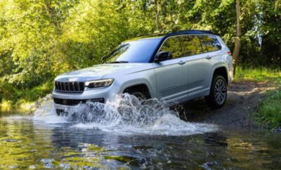 Silver SUV splashes through a shallow creek in a forest.
