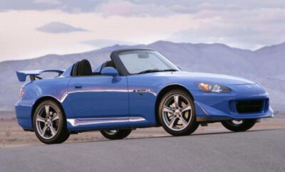 A blue convertible sports car parked with mountains in the background.