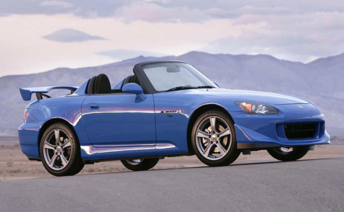 A blue convertible sports car parked with mountains in the background.
