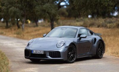A sleek gray sports car parked outdoors among trees.