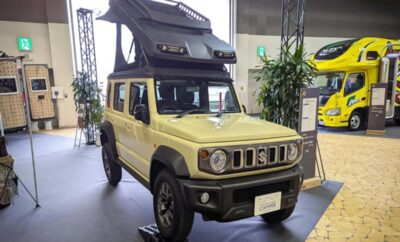 Yellow off-road vehicle with rooftop tent displayed indoors.