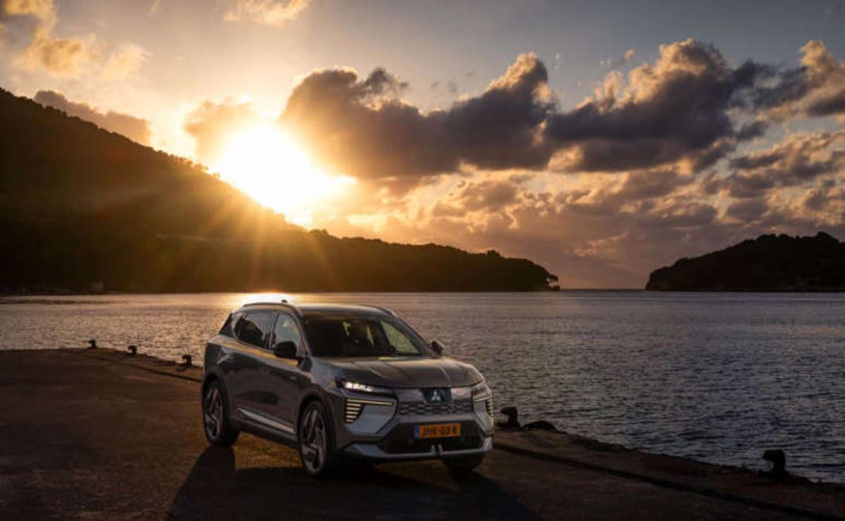 SUV parked by the water at sunset with glowing clouds.