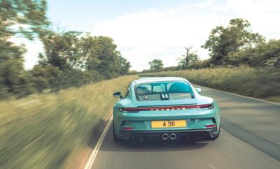 A teal sports car driving down a rural road surrounded by trees.