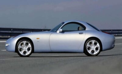 Silver classic sports car parked on a road under a clear sky.