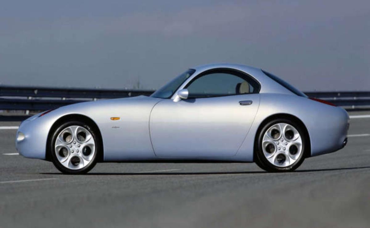Silver classic sports car parked on a road under a clear sky.