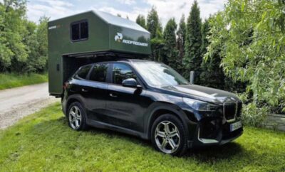 A sleek black SUV parked on grass in front of a green camper.