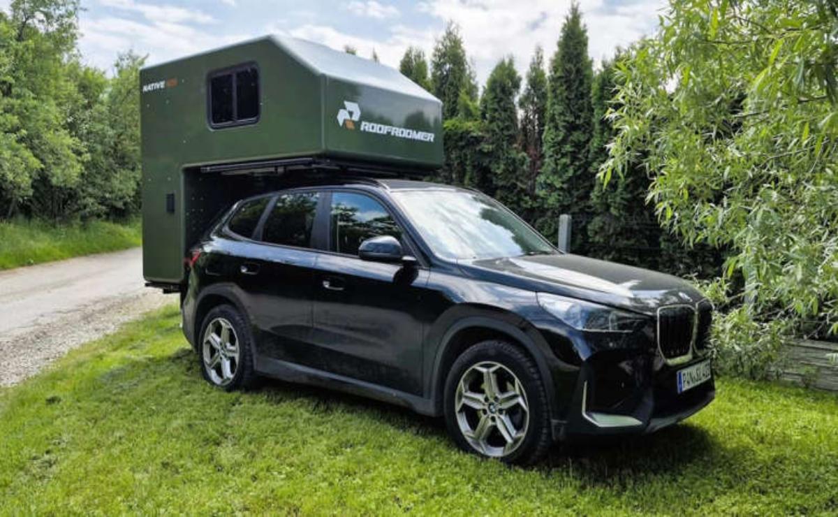 A sleek black SUV parked on grass in front of a green camper.