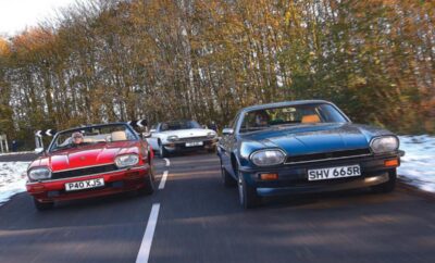Three classic cars parked side by side in an outdoor lot during autumn.