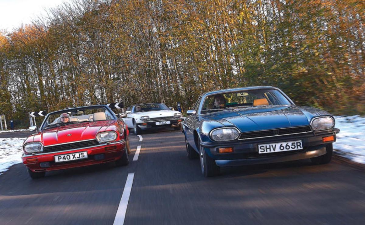 Three classic cars parked side by side in an outdoor lot during autumn.