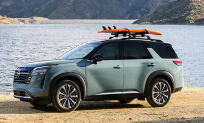 A green SUV parked by a lake with a surfboard on the roof rack.