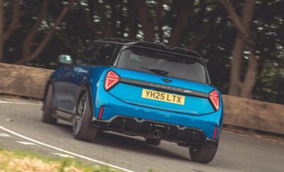 Blue sports car driving on a curved road surrounded by trees.