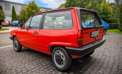 Classic red compact car parked on a cobblestone street.