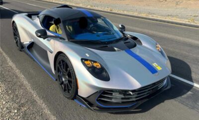 Silver sports car with blue and yellow racing stripes on a desert road.