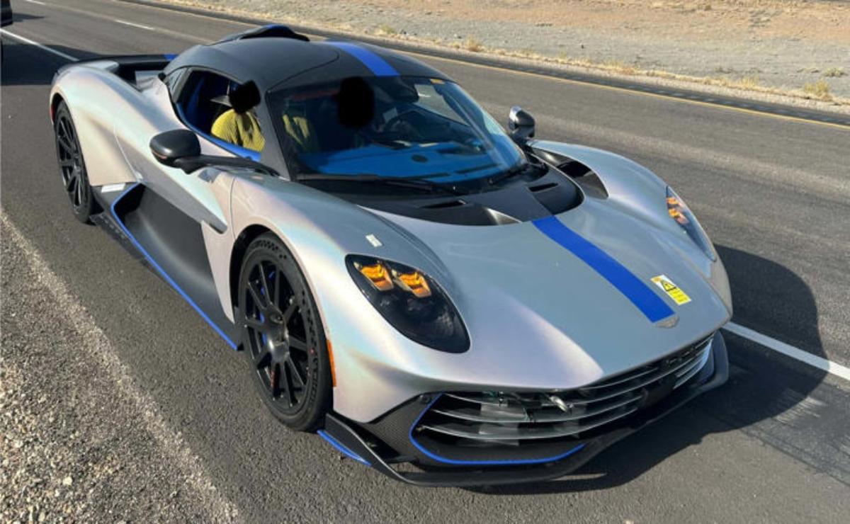 Silver sports car with blue and yellow racing stripes on a desert road.