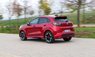 Red compact SUV driving on a road with trees in the background.