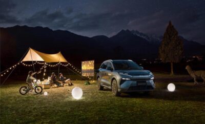 A car parked near a lit-up tent under a twilight sky.