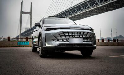 A sleek black SUV parked under a modern bridge on a gray day.