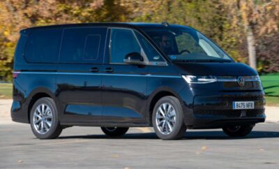 A sleek black minivan driving on a road with trees in the background.