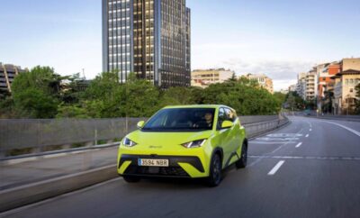 Bright green compact car driving on an urban road with a tall building in the background.