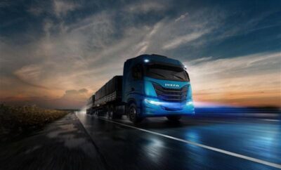 A sleek blue truck driving on a road during sunset.